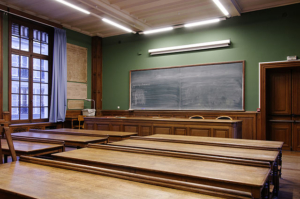 empty classroom with chalkboard in the forefront and wooden desks 