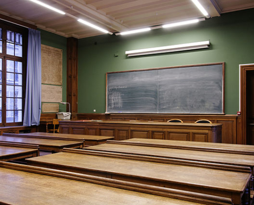 empty classroom with chalkboard in the forefront and wooden desks