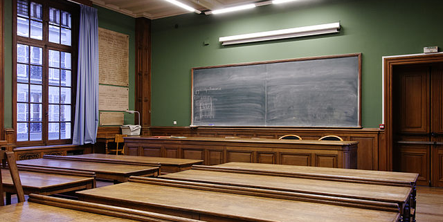 empty classroom with chalkboard in the forefront and wooden desks